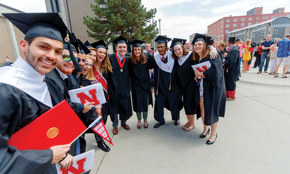 Group of students smiling for the camera in their caps and gowns at commencement.