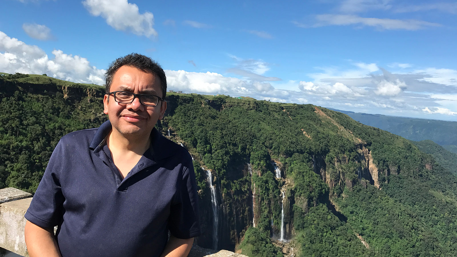 Dr. Francisco-Munoz-Arriola standing in front of a picturesque scene of mountains, forests and waterfalls.