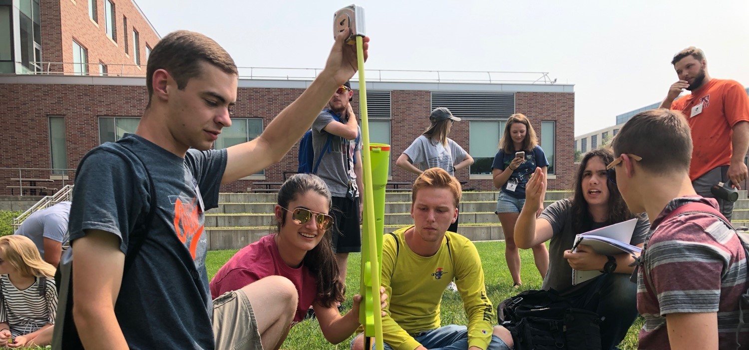 5 engineering students collaborate outside with a tennis ball launcher