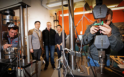 Jongwan Eun, Yuris Dzenis and Seunghee Kim pose in Dzenis’ lab as Benjamin Bashtovoi and Mikhail Kartashov test carbon-fiber samples
