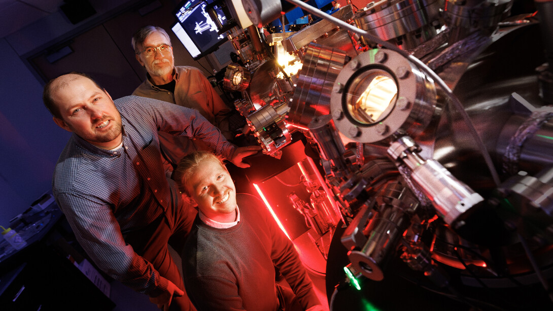 Craig Zuhlke (left) and George Gogos (back), co-directors of the Center for Electro-Optics and Functionalized Surfaces, and Graham Kaufman, doctoral student in electrical engineering, pose with the Leybold ultra-high vacuum laser surface processing and materials analysis system in the CEFS lab in the Engineering Research Center. (University Communicaton and Marketing photo)