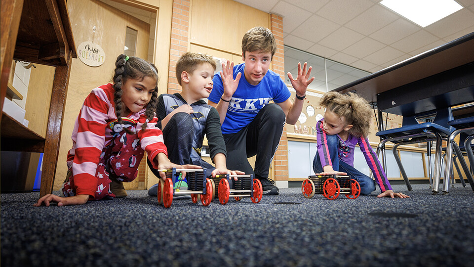 Spencer Knight gets three students and their rubber-band powered cars lined up for a race at Riley Elementary School in Lincoln. (Craig Chandler / University Communication and Marketing)