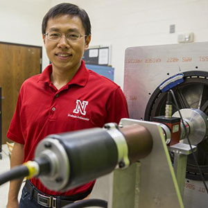 Jie Cheng, doctoral student in electrical engineering, stands next to the partial prototype of a wind turbine system that research suggests could yield 8.5 percent more electricity than conventional counterparts. (Troy Fedderson / University Communications)