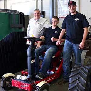 Roger Hoy (from left), Caleb Lindhorst and Luke Prosser show off a tractor designed by students for a 2014 engineering competition. Lindhorst was involved in a December 2013 auto accident and support from Hoy and Prosser has helped him return to classes at UNL. (Photo by Troy Fedderson / University Communications)