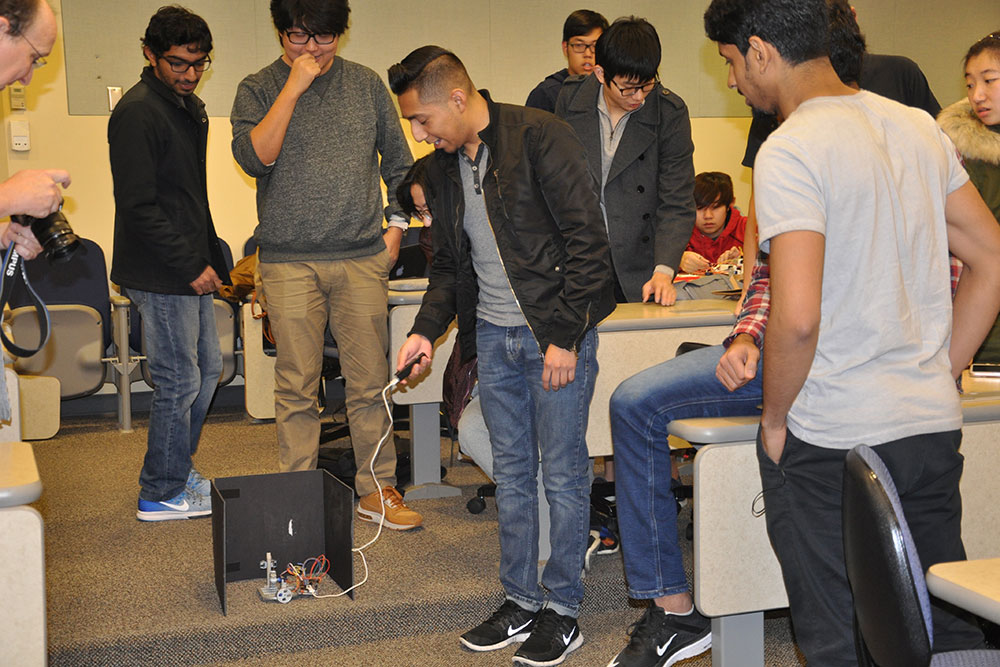 Students in ELEC 121 try to make a device they created shoot a rubber band from inside a three-sided box.