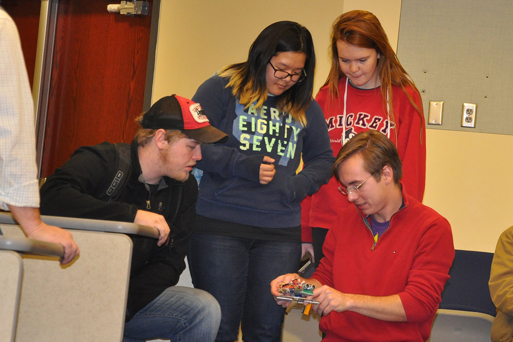 Students in ELEC 121 work on a device they created to shoot a rubber band from inside a three-sided box.