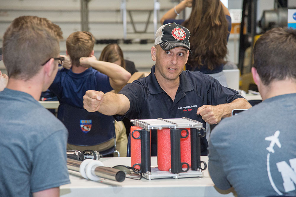 A member of the dive team from the Johnson Space Center's Neutral Buoyancy Laboratory discusses the operation of a gap spanner boom prototype with the designers from UNL's Air and Space Research Team.