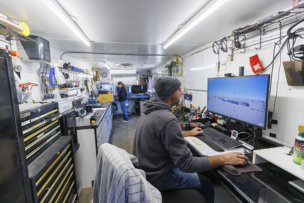 Jim Holloway and Karla Lechtenberg work on the computer connections and camera views in a trailer rigged to record the information at the crash test site. (Craig Chandler / University Communication)