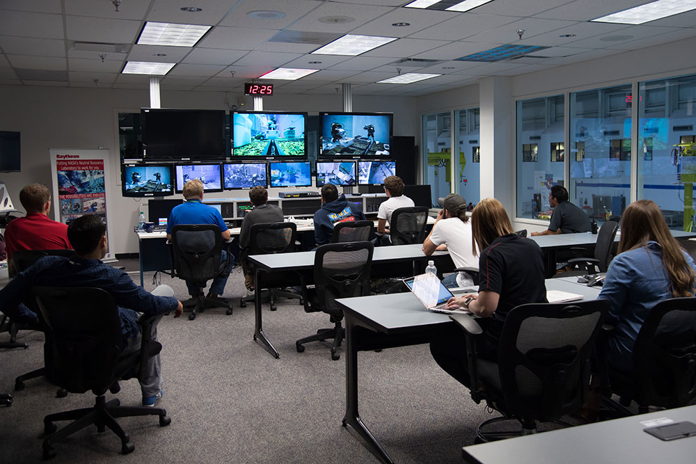 Members of the Nebraska Air and Space Research team watch from the Johnson Space Center control room as divers test their anchoring device in the Neutral Buoyancy Laboratory pool.