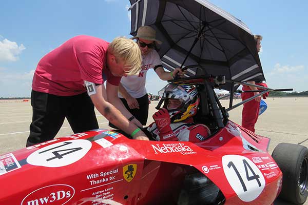 The crew uses an umbrella to keep the driver cool as they work on the Husker Motorsports Formula SAE car before Friday's autocross run at Lincoln Airpark.