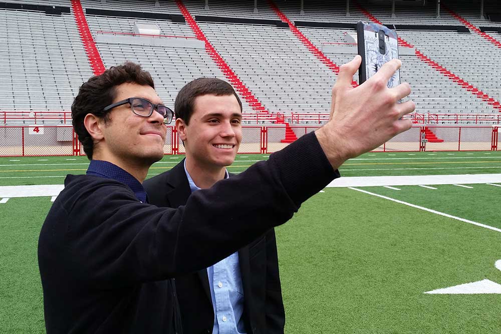 After taking part in the group picture on the field at Memorial Stadium, two engineering students take a selfie before returning to the Senior Design Showcase.