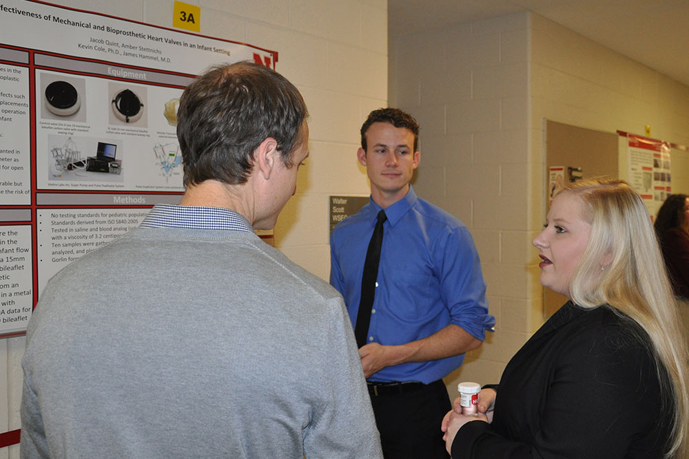 Amber Stettnichs (right) and Jacob Quint (center) explain their research to assistant professor Ryan Pedrigi.