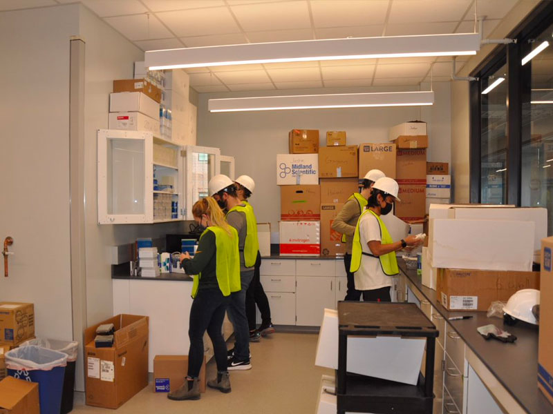 Students help unload supplies into a new second floor lab of the engineering research center while the hallway of the Engineering Research Center is lined with new lab spaces and windows. 