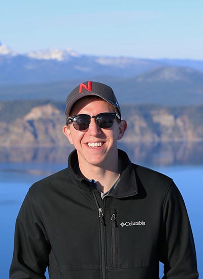 UNL Civil Engineering Alumni Bryan Kubitschek posing in front of a lake and mountain scene.