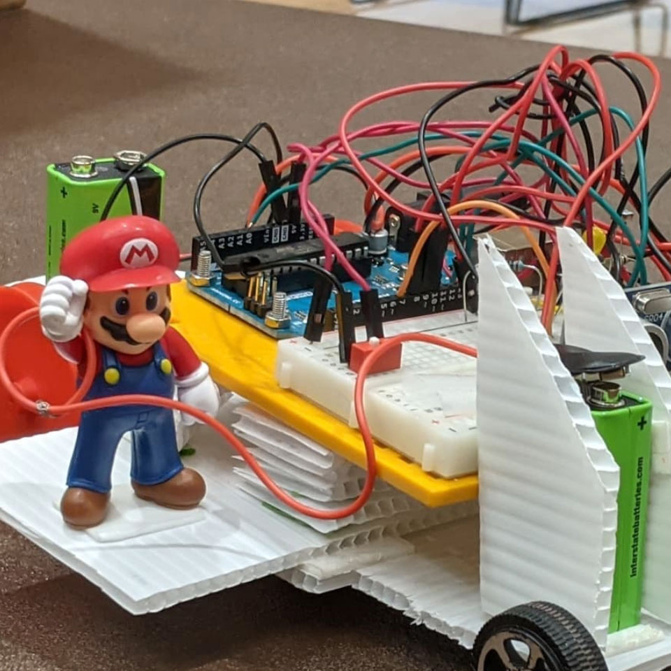 A battery operated toy vehicle designed by students that has a figure of Super Mario standing on it is on display at E-Day in the Nebraska East Union.