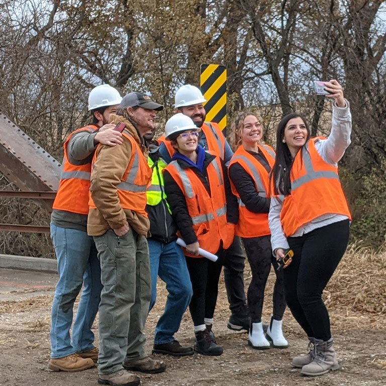 Group of students with orange safety vests on pose for a group selfie.