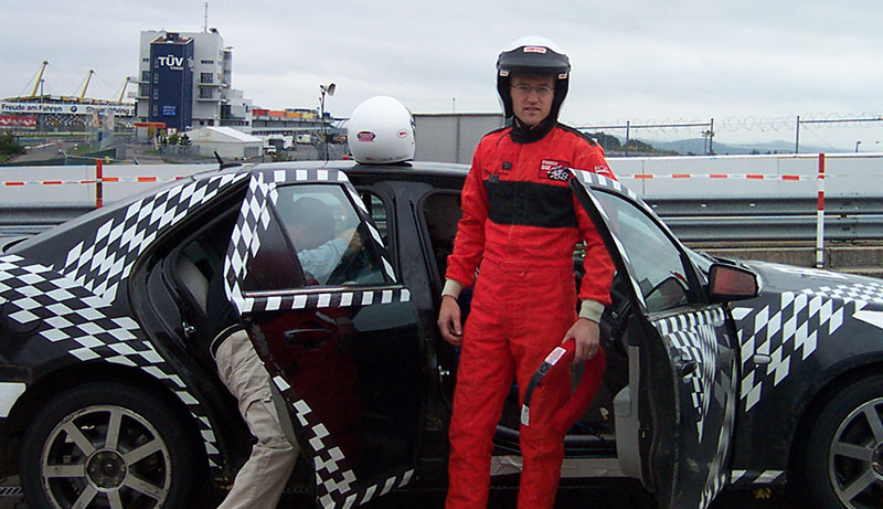 Alumni Master Jeff Lundy in full race gear standing in front of a race car.
