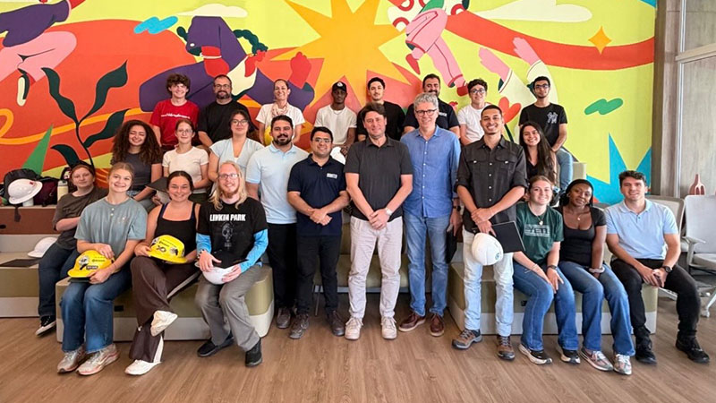 Group of people smiling in front of a colorful mural, some holding hard hats.