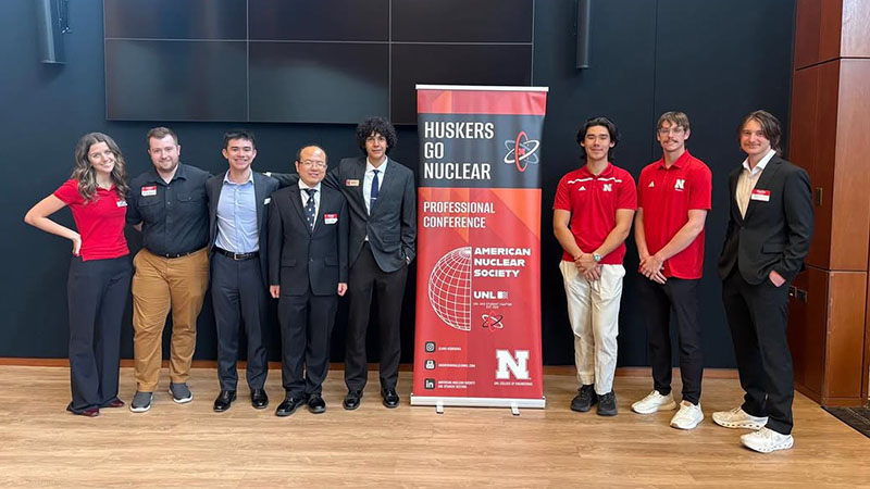 Group of people standing beside a "Huskers Go Nuclear" conference banner in a professional setting.