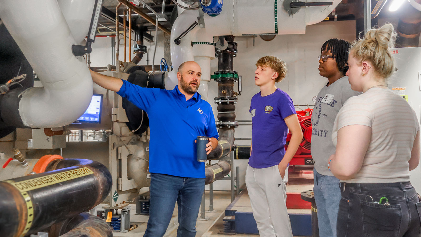 Group listening to a man explaining machinery in an industrial setting.