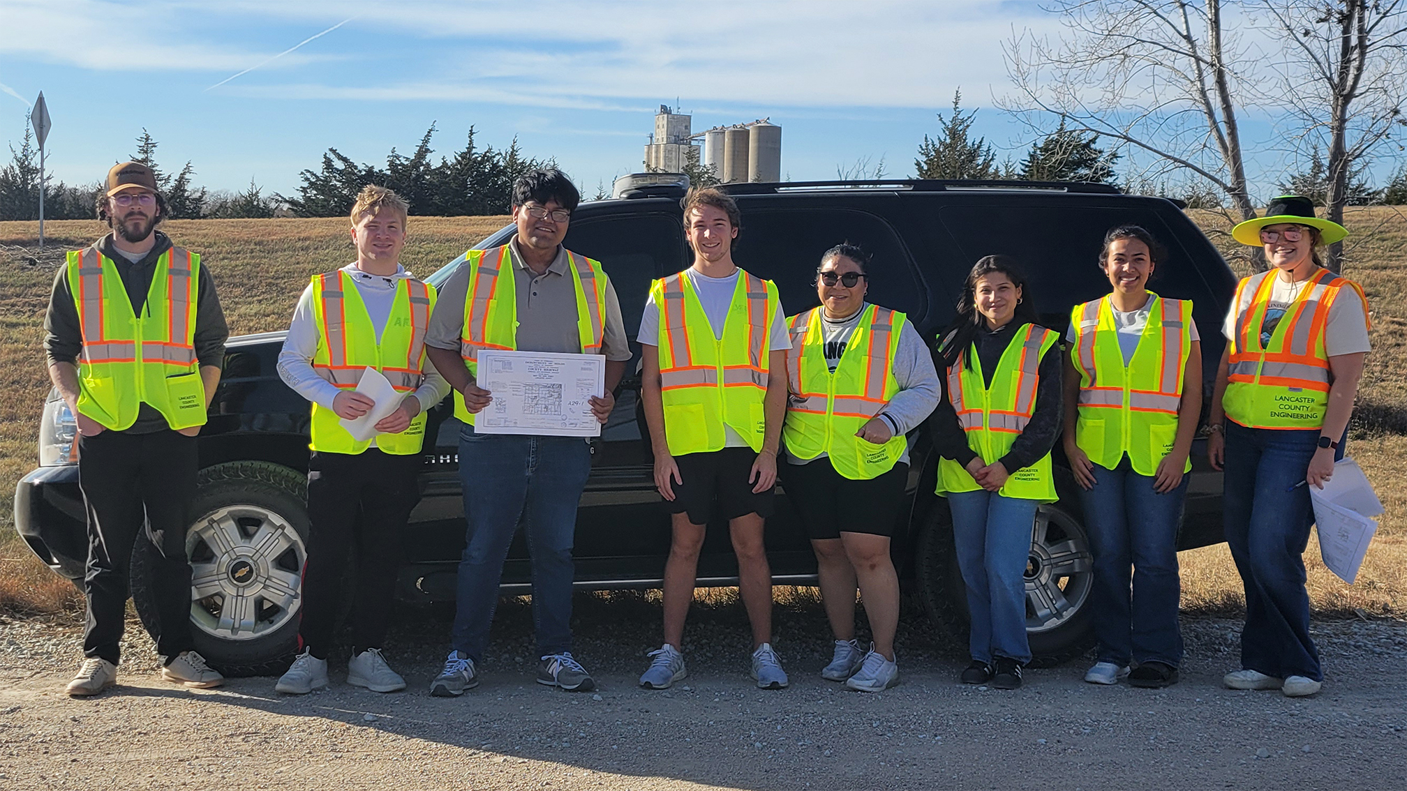 Group of people in reflective vests standing in front of a black SUV outdoors.