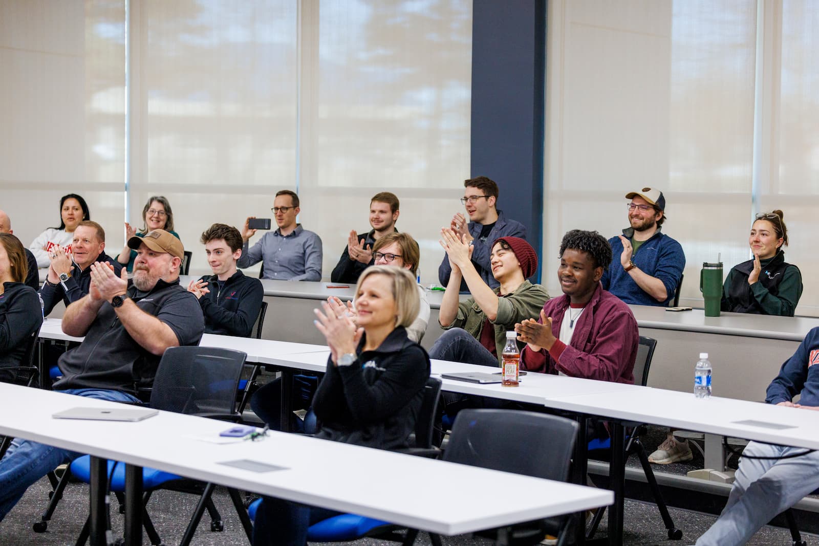 A group of people applauding while seated in three table rows.