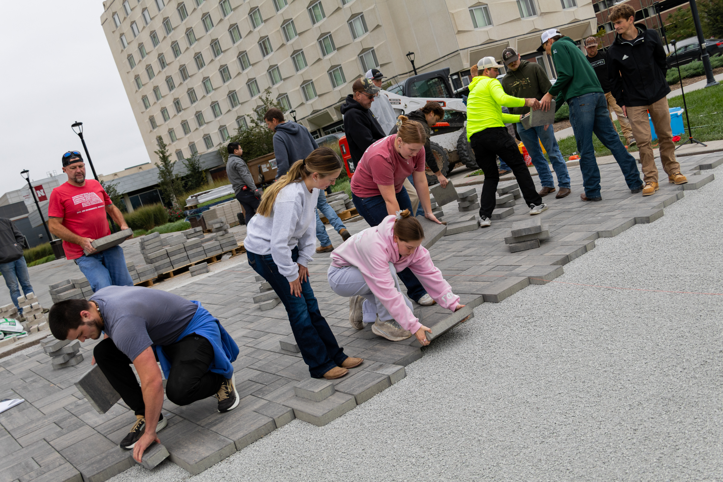 People laying paving stones in an outdoor area near a large building.
