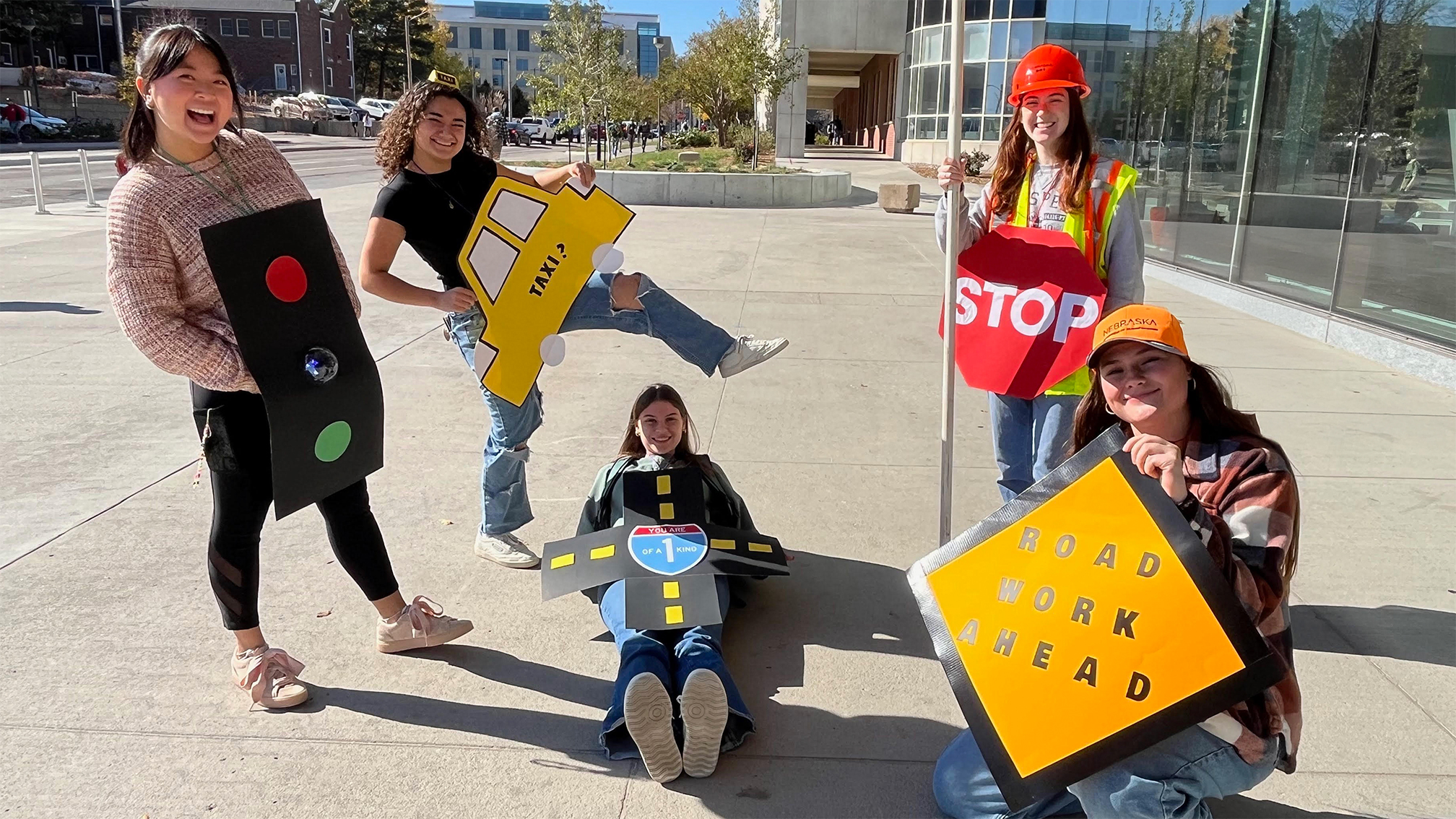 People in traffic-themed costumes pose outdoors on a sunny day near a modern building.