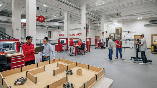 Robotics lab with students working on projects and machinery in a bright, spacious workshop.