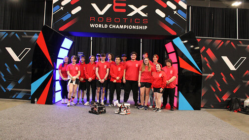 Group of students in red shirts smiling under a "VEX Robotics World Championship" sign.