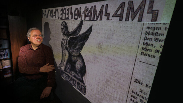 Peter Revesz poses in front of artwork of an ancient sphinx artifact