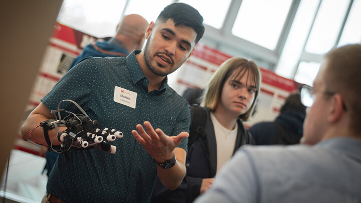 Person demonstrating a robotic glove to others in a bright room.