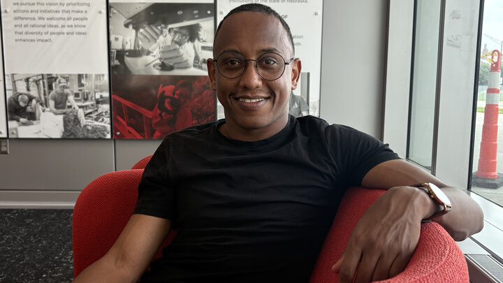 Brhanu Fentaw, a biomedical engineering doctoral student at the University of Nebraska–Lincoln, smiles as he sits in a red padded chair. He is wearing a black T-shirt, watch and glasses.