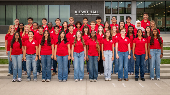 Forty University of Nebraska–Lincoln students in red polos and blue jeans pose for a group photo in front of Kiewit Hall.