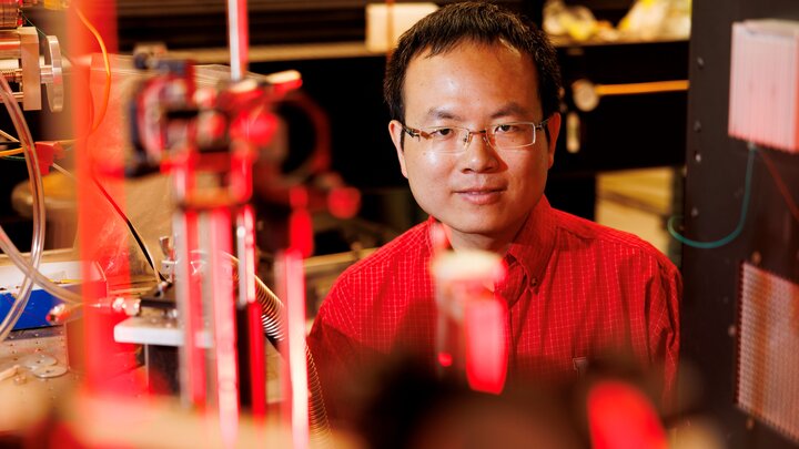 Lab setting with red laser equipment and blurred background. Bai Cui, professor of Mechanical and Materials Engineering