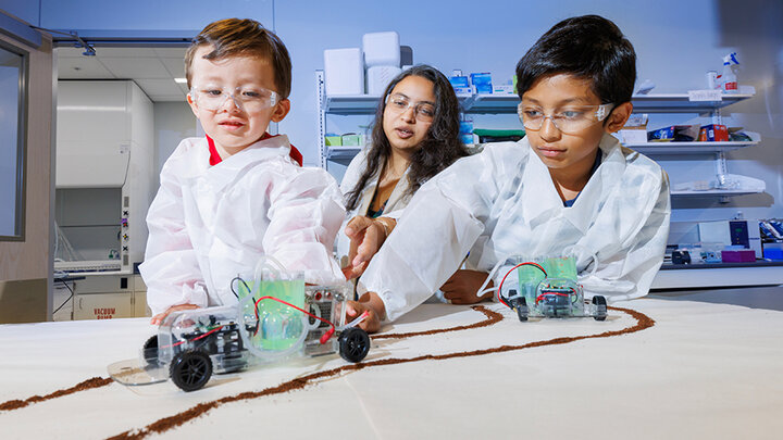 Shudipto Dishari helps Rafael López (left) and Sreyan Saha (right) as they play with cars powered by green energy using biomaterials.