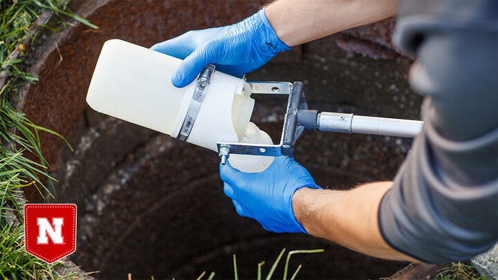 A graduate student collects a wastewater sample from a sewer connected to Harper Residence Hall.