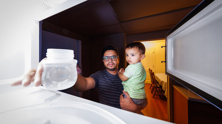 Kazi Albab Hussain (left) holds his son while removing a plastic container of water from a microwave.