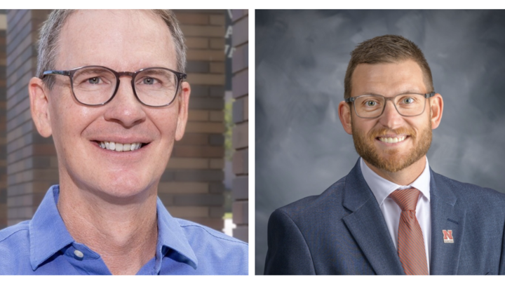 Two men wearing glasses; one in a blue shirt, the other in a suit.