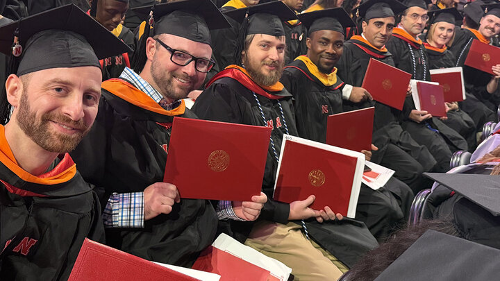 Gradauates sitting and holding their diplomas 