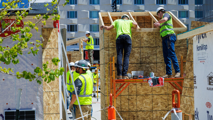 Construction workers building a wooden structure outdoors, wearing safety gear.
