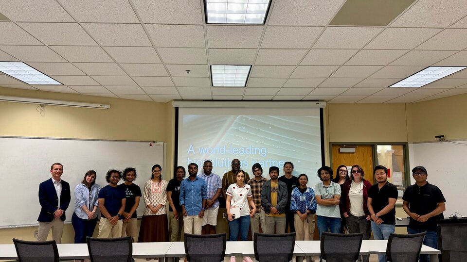 Group of people standing in a classroom with a presentation screen in the background.