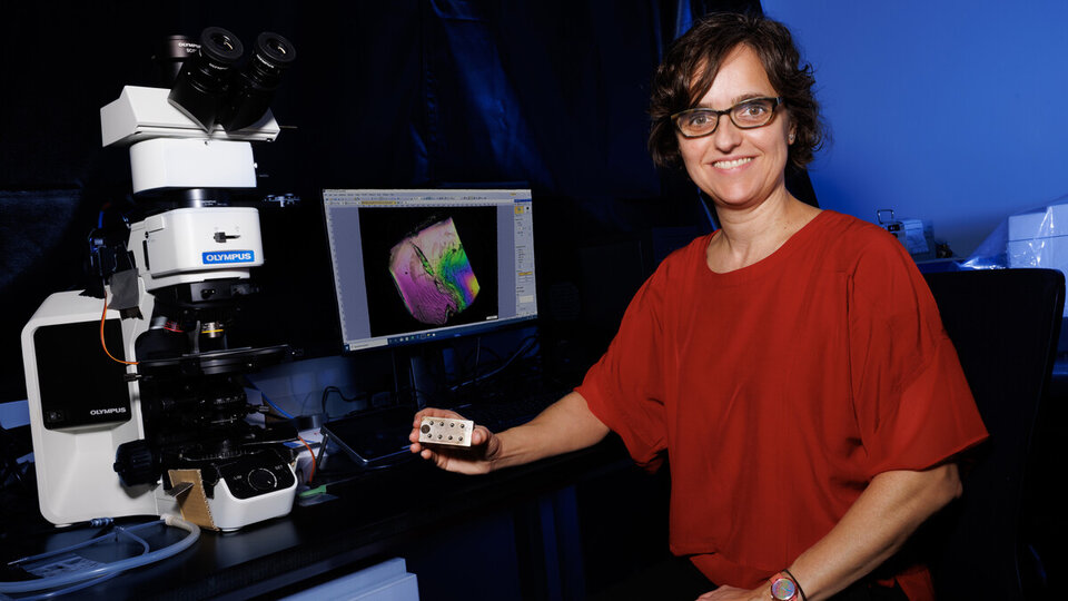 Female professor sits by large miscroscope and computer