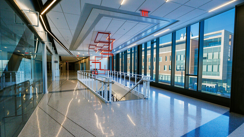 Bright modern hallway with large windows, glossy floors, red geometric light fixtures, and staircase.