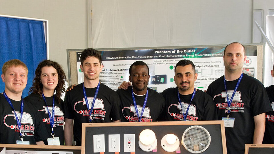Group of people wearing matching black shirts, standing in front of a booth with an energy-saving display.
