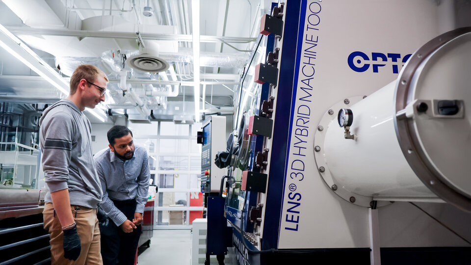 Two people examining a large 3D hybrid machine tool in a bright industrial setting.