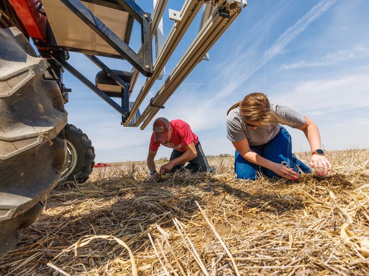 Two students on a field digging through the dirt beside a robotic planter.