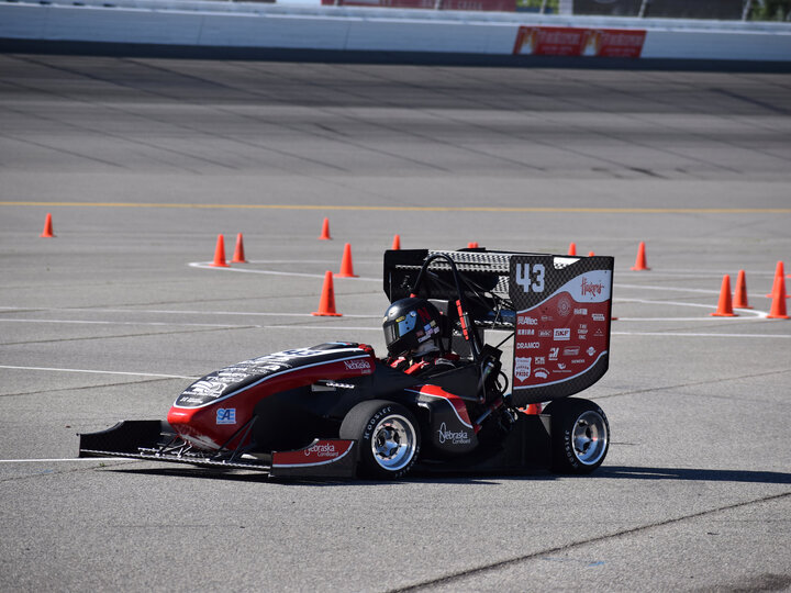Formula race car maneuvering through orange cones on a paved track.