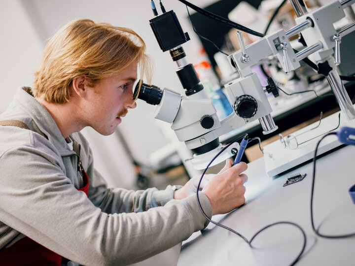A student uses a microscope to aid in precision soddering.