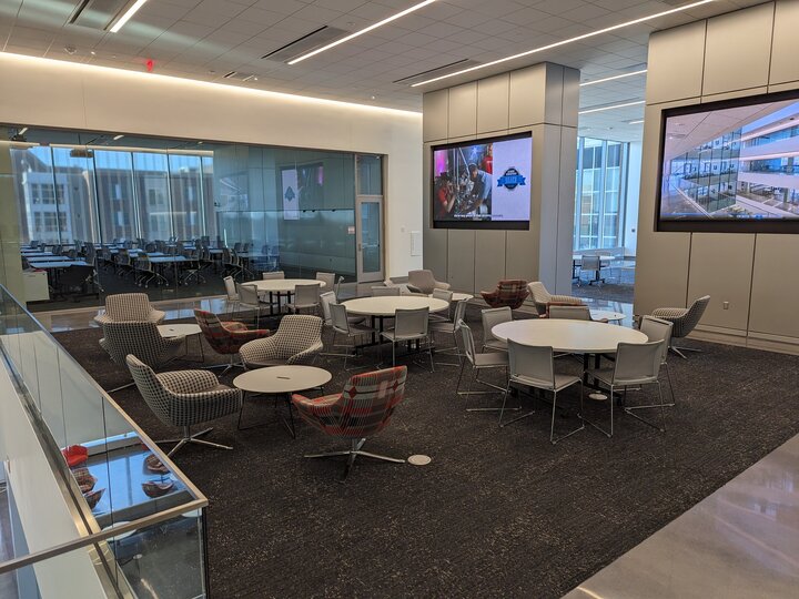 Modern office lounge with round tables, chairs, and large screens on the walls.